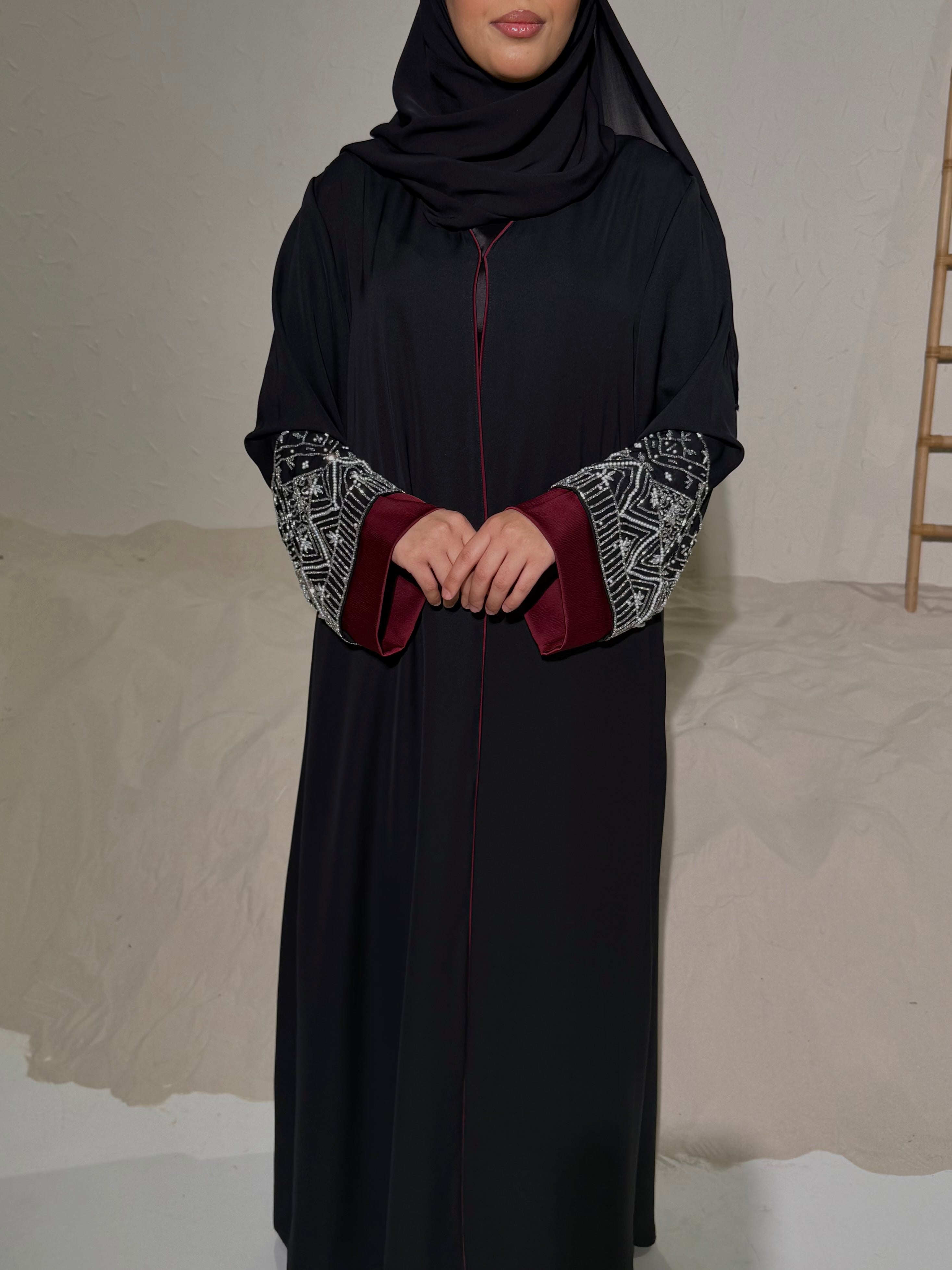 Woman wearing a black abaya with patterned sleeves against a neutral background